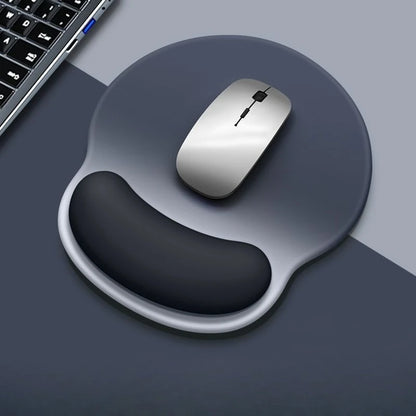 Gray mouse on a dark gray mouse pad with wrist rest, next to a keyboard on a gray surface.